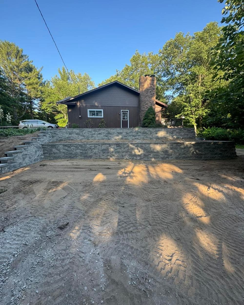 House with stone patio under construction, surrounded by trees and blue sky.