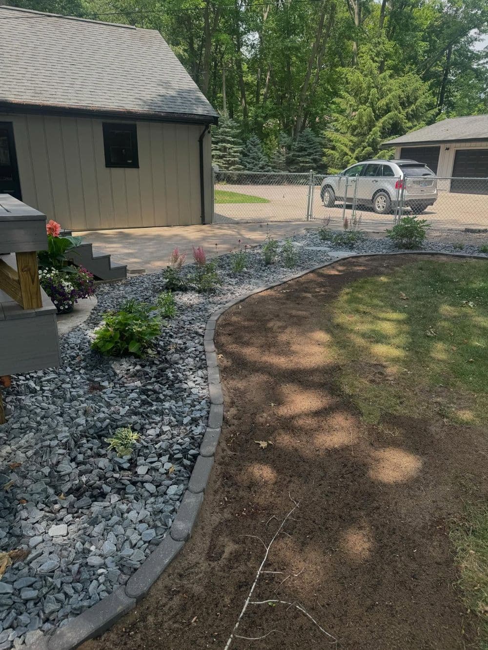 Landscaped yard with gravel border, plants, and a parking area in a suburban setting.