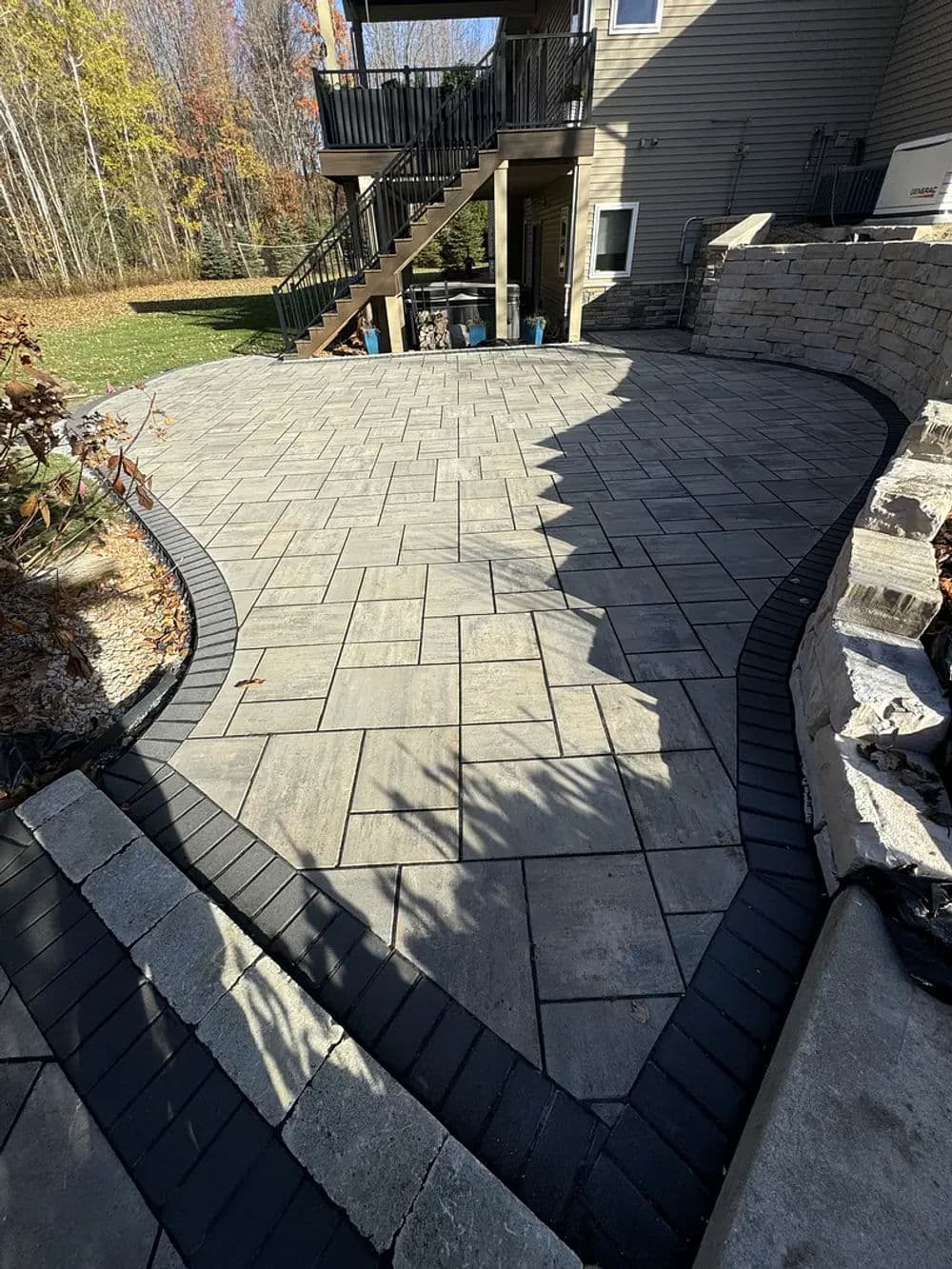 Paved outdoor patio with patterned stones and black borders, surrounded by greenery.
