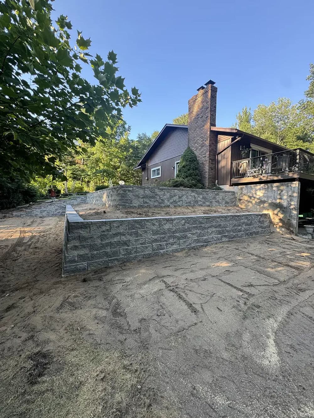 House with stone retaining wall and cleared yard, surrounded by greenery and trees.