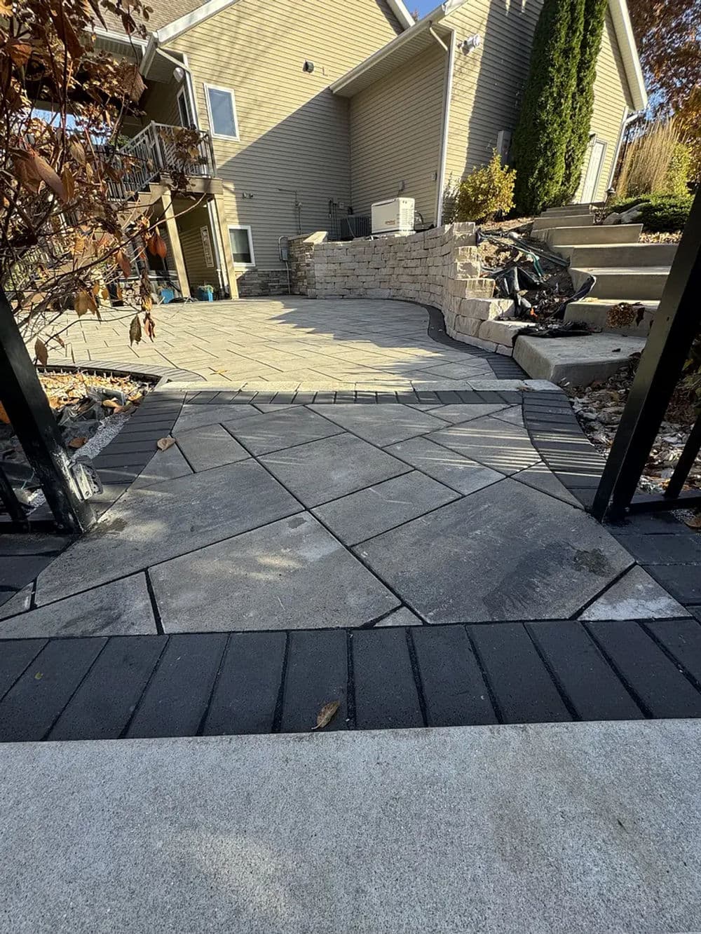 Paved walkway leading to a house with steps and landscaping in the background.