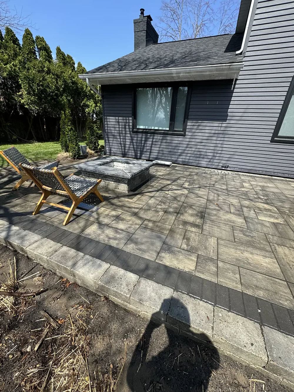 Patio area with stone pavers, seating chairs, and a fire pit next to a house.