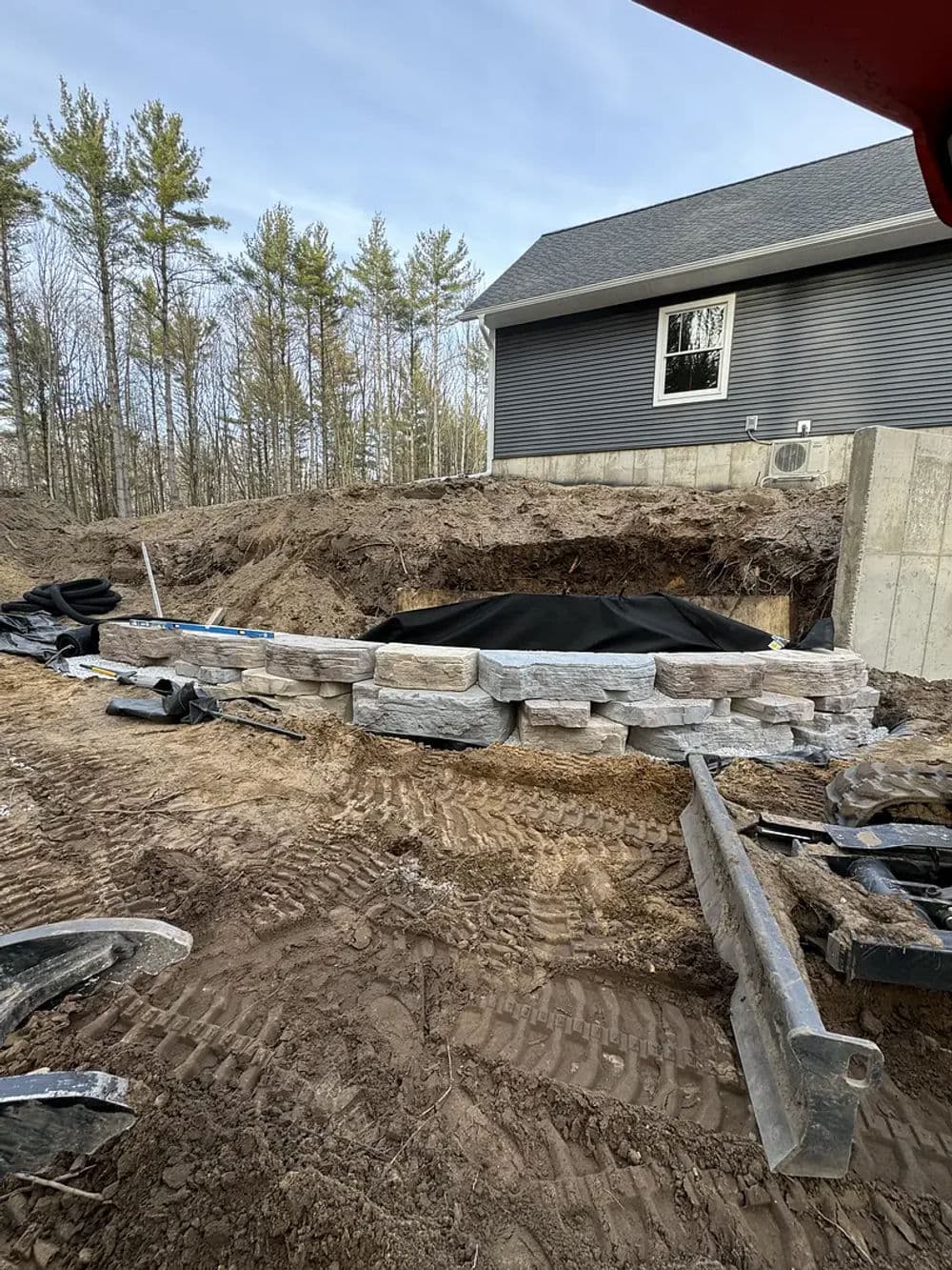 Stone retaining wall under construction at a residential property surrounded by trees.